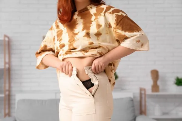 Image of woman trying to do her trousers up after pregnancy weight gain Shoreham by Sea
