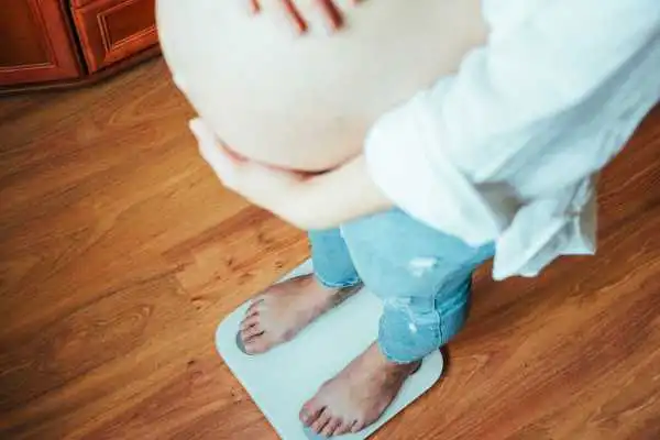 Image of woman weighing herself and experiencing weight gain through pregnancy Shoreham by Sea